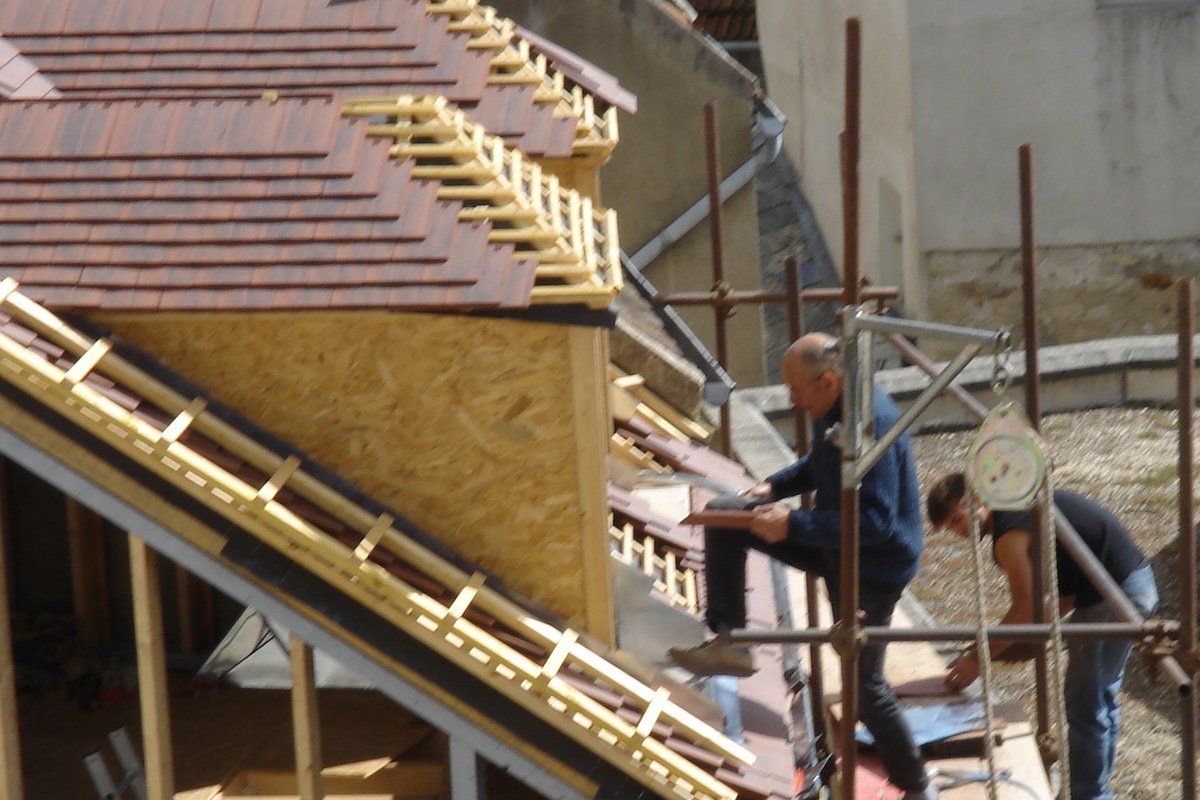 Deux couvreurs posant des tuiles sur une toiture en rénovation